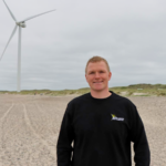 Her ses Morten Rauhe, driftsleder hos Hvide Sande Fjernvarme, foran to af de tre vindmøller, de har opsat ved den jyske vestkyst