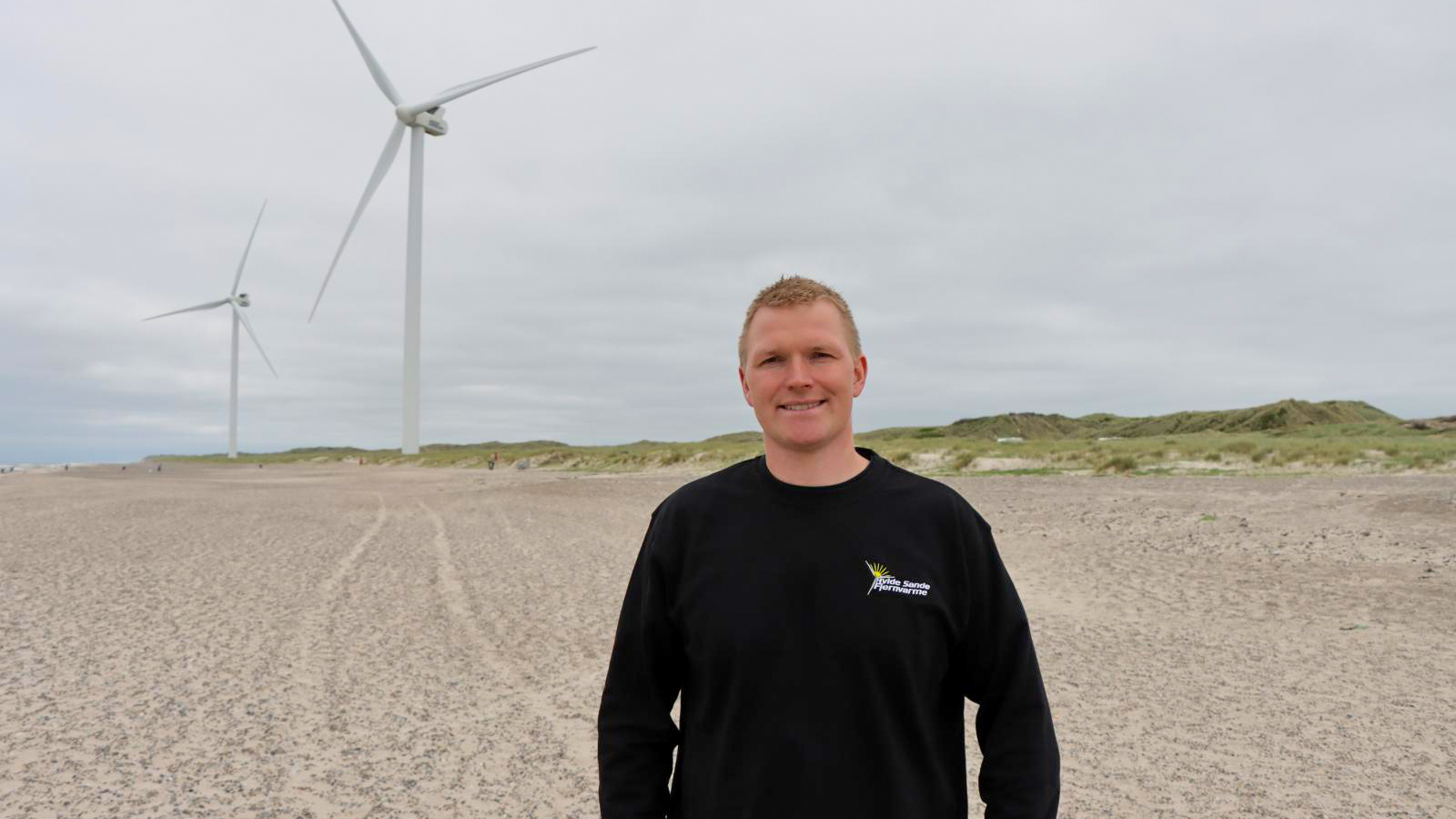Her ses Morten Rauhe, driftsleder hos Hvide Sande Fjernvarme, foran to af de tre vindmøller, de har opsat ved den jyske vestkyst
